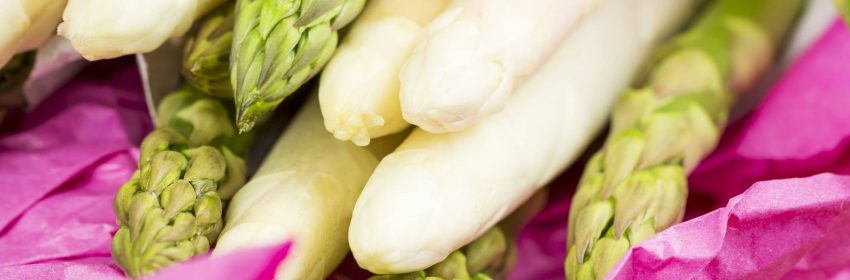 Bundle of fresh green and white asparagus spears or shoots wrapped in colorful pink paper on a wooden table ready for steaming or boiling